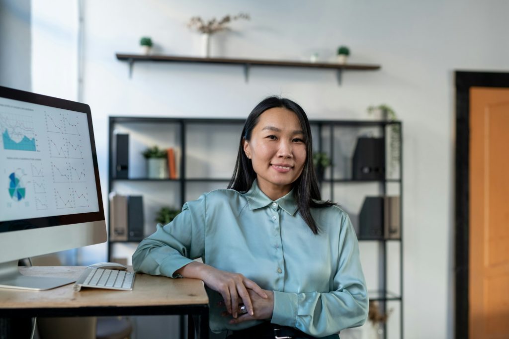 Young Asian economist in smart casualwear standing by workplace